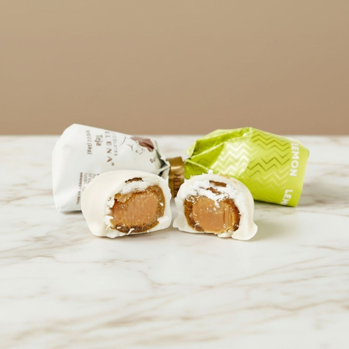 Lemon Teja Bonbon cut open showing lemon fondant filling, with Helena Chocolatier wrappers on marble