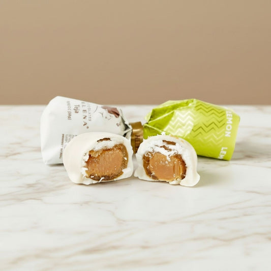 Lemon Teja Bonbon cut open showing lemon fondant filling, with Helena Chocolatier wrappers on marble