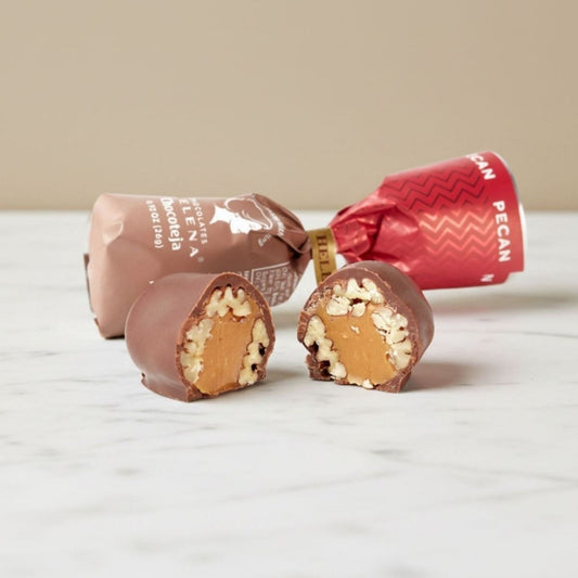 Pecan Chocoteja Bonbon cut open showing pecan and manjar blanco filling, with Helena Chocolatier wrappers on marble