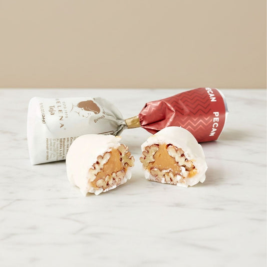 Pecan Teja Bonbon cut open showing pecan and fondant filling, with Helena Chocolatier wrappers on marble