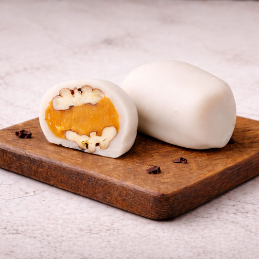 Pecan Teja Bonbon whole and cut in half showing pecan and fondant filling on a wooden board