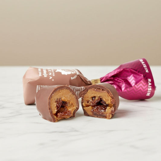 Raisin Chocoteja Bonbon cut open showing raisins and manjar blanco filling, with Helena Chocolatier wrappers on marble