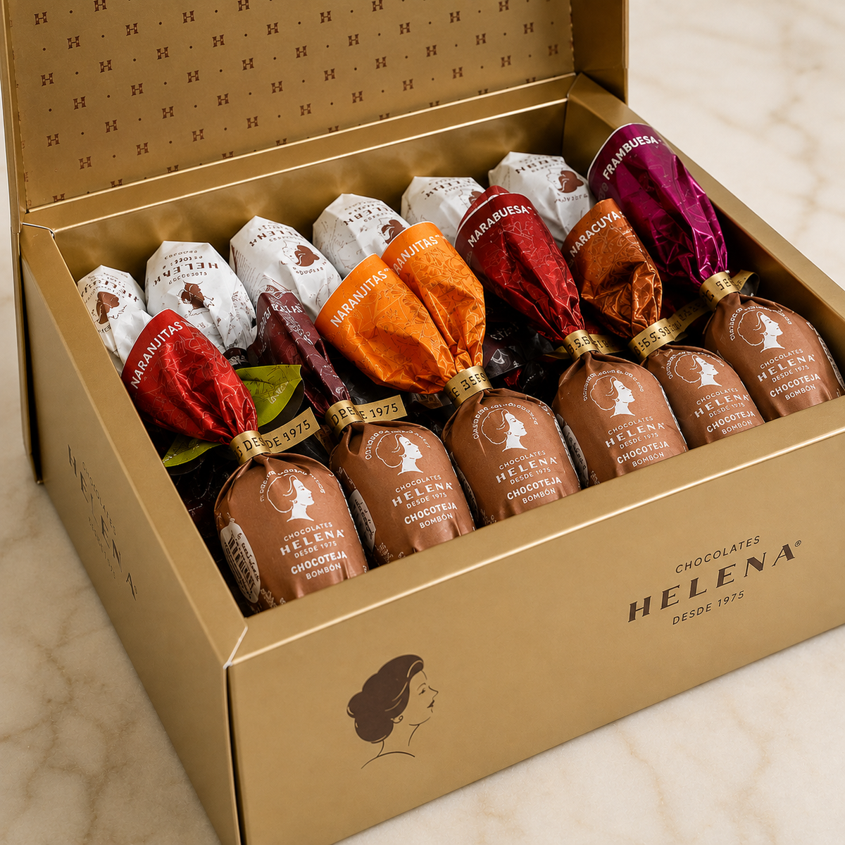 Helena Chocolatier Golden Gift Box open showing 36 assorted Teja and Chocoteja bonbons – flavors include Naranjitas, Narabuesa, Naracuya, Frambuesa and Chocoteja, handcrafted since 1975
