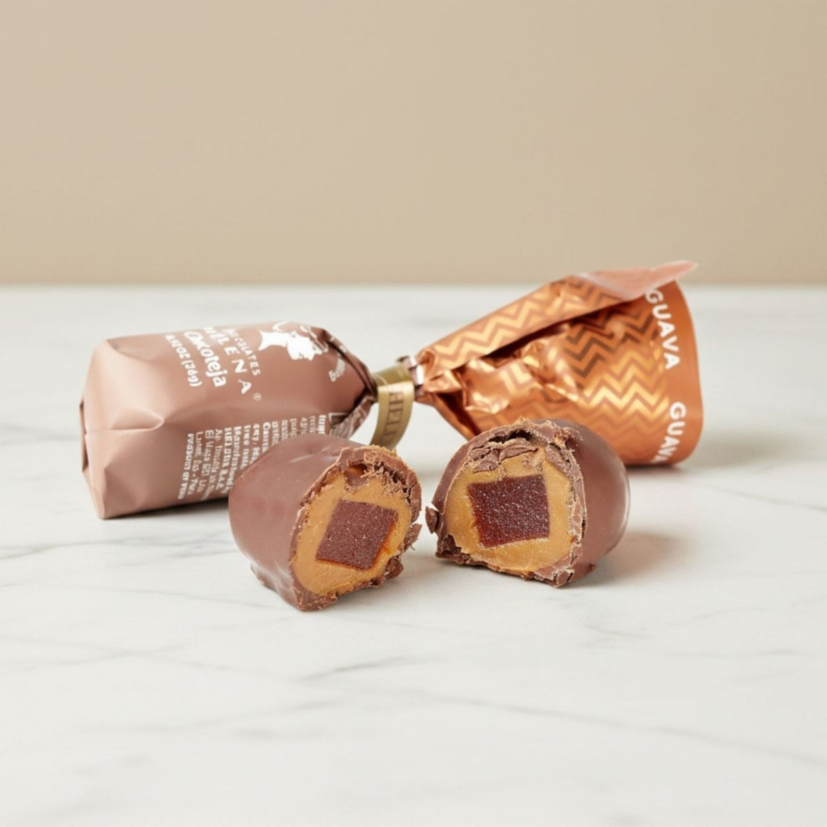 Guava Chocoteja Bonbon cut open showing guava paste and manjar blanco filling, with Helena Chocolatier wrappers on marble