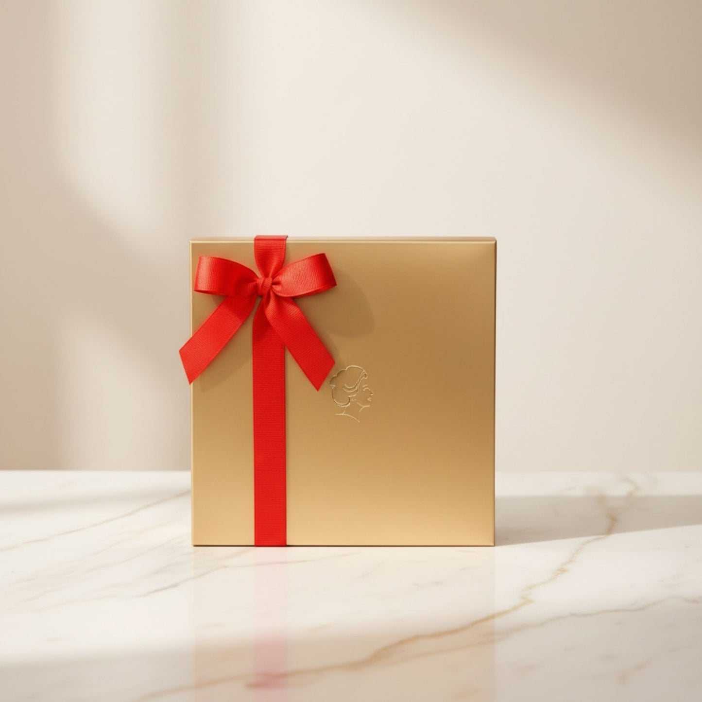 Helena Chocolatier gold gift box with red satin ribbon on marble surface