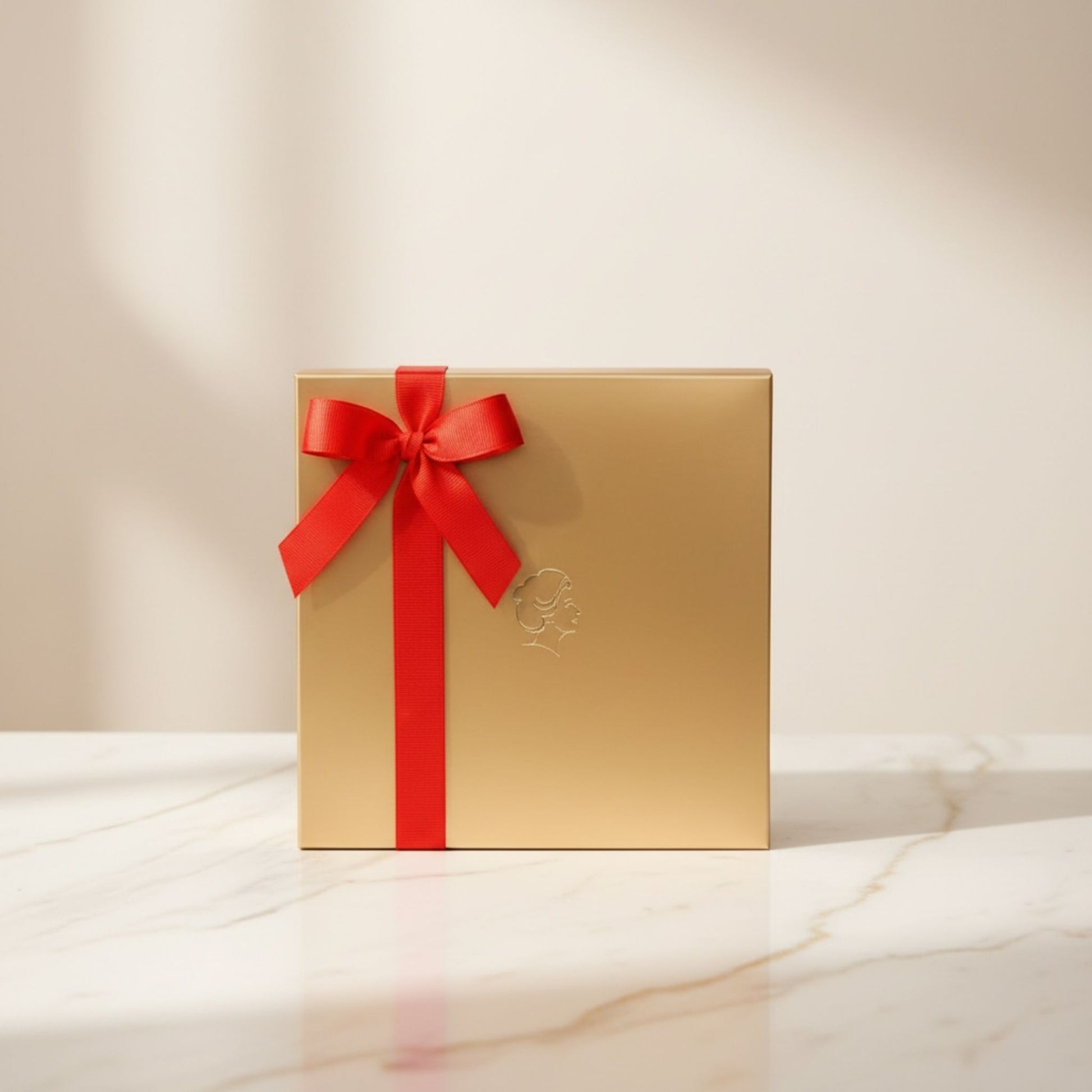 Helena Chocolatier gold gift box with red satin ribbon on marble surface