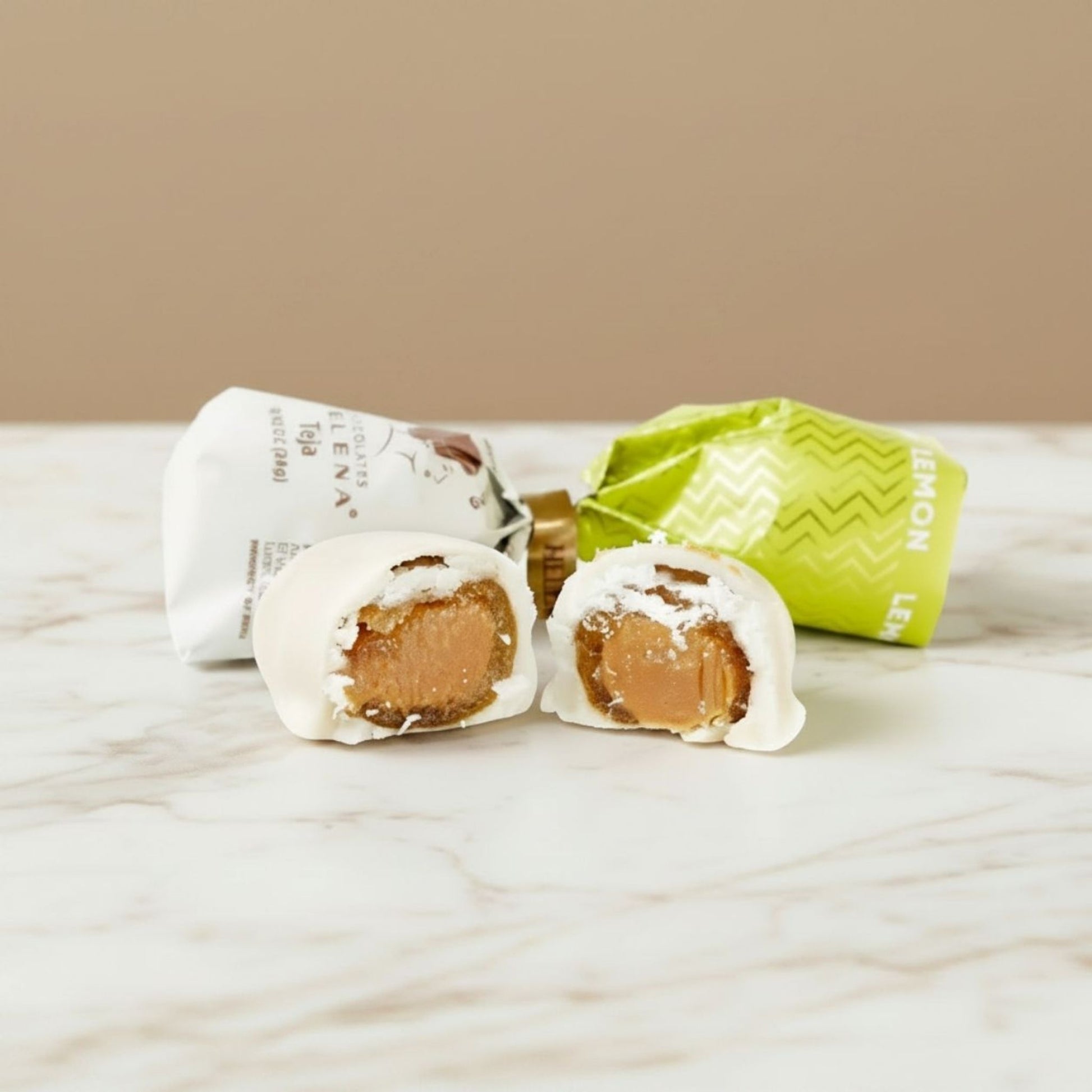  Lemon Teja Bonbon cut open showing lemon fondant filling, with Helena Chocolatier wrappers on marble
