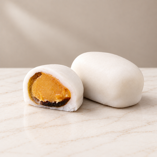 White-coated citrus Tejas, one whole and one cut open to reveal the golden filling, on white marble