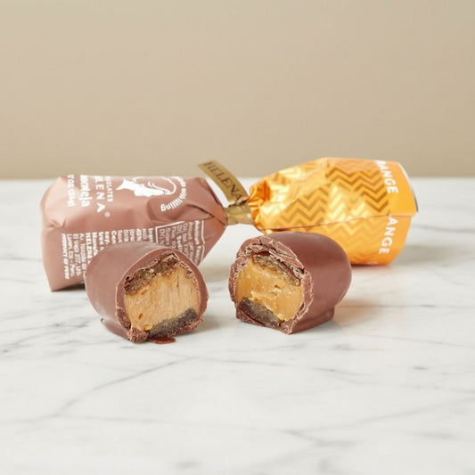 Orange Chocoteja Bonbon cut open showing candied orange peel and manjar blanco filling, with Helena Chocolatier wrappers on marble