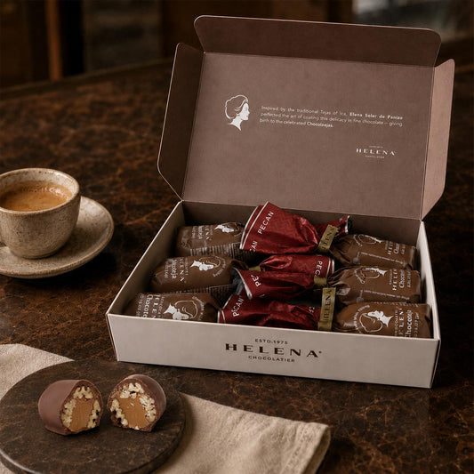 Open Helena Chocolatier gift box with 6 Pecan Chocoteja Bonbons in red and brown wrappers, with a cut bonbon showing pecan and manjar blanco filling, alongside an espresso cup"