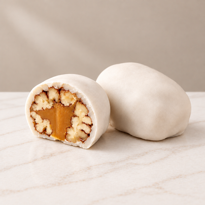 White-coated Pecan Tejas, one whole and one cut open to reveal pecans and golden filling, on white marble