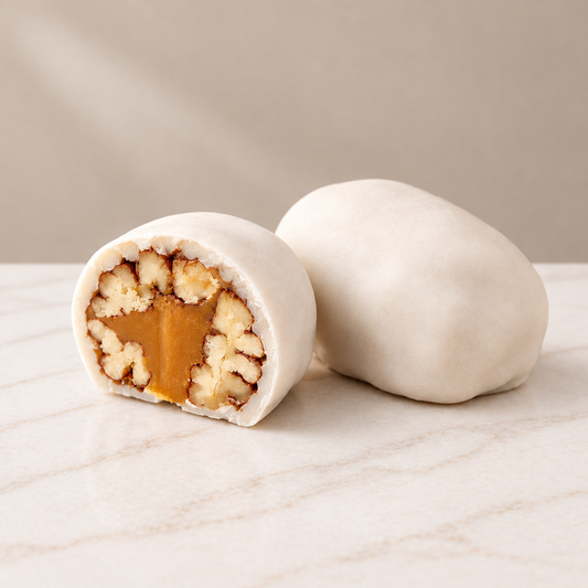 White-coated Pecan Tejas, one whole and one cut open to reveal pecans and golden filling, on white marble