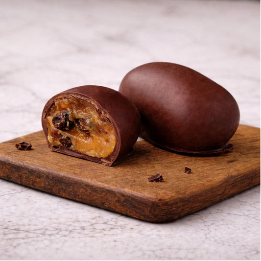 Raisin Chocoteja Bonbon whole and cut in half showing raisins and manjar blanco filling on a wooden board