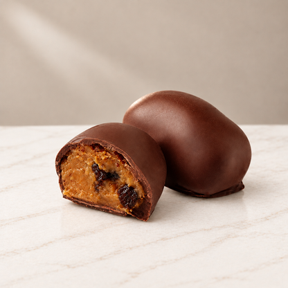 aisin Chocoteja Bonbons, one whole and one cut open to reveal raisins and golden filling, on white marble