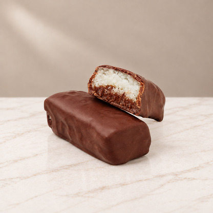 Coconut Toffee Bonbon cut open showing coconut toffee filling, with Helena Chocolatier wrappers on marble